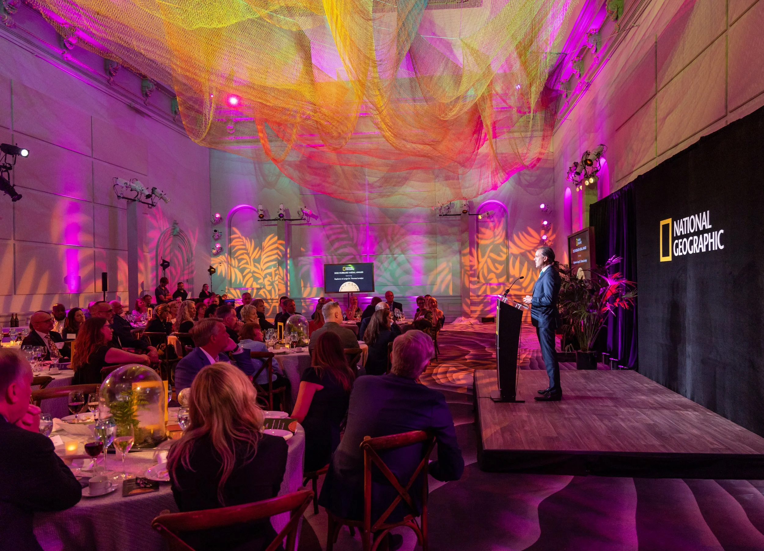 Seated guests watching a man on stage in from of a National Geographic presentation during a National Geographic annual gala, produced by Stratus Firm, an event production company located in Washington DC