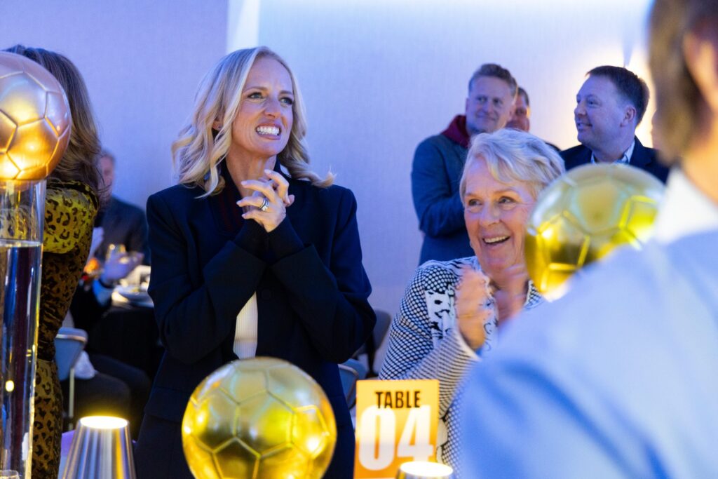 People at a table laugh and smile and watch the stage at the 2025 Play for Good Gala
