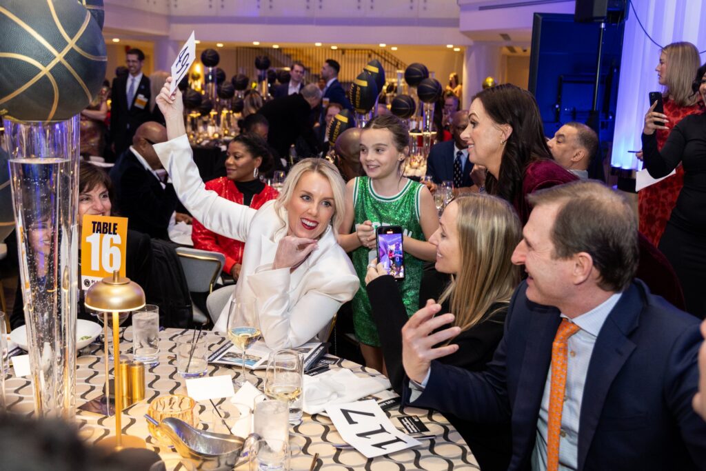 People chat together as one woman holds up her bidding number at an auction during the Play for Good gala