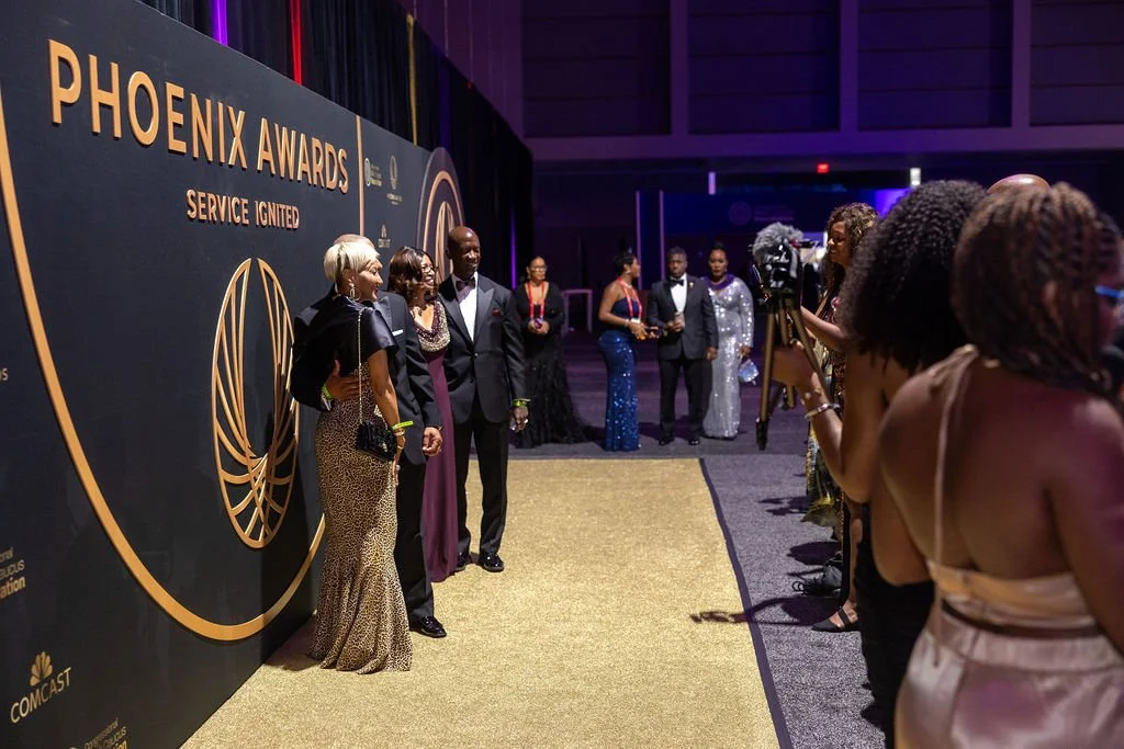People stand in front of a photo op and smile at the Phoenix Awards.