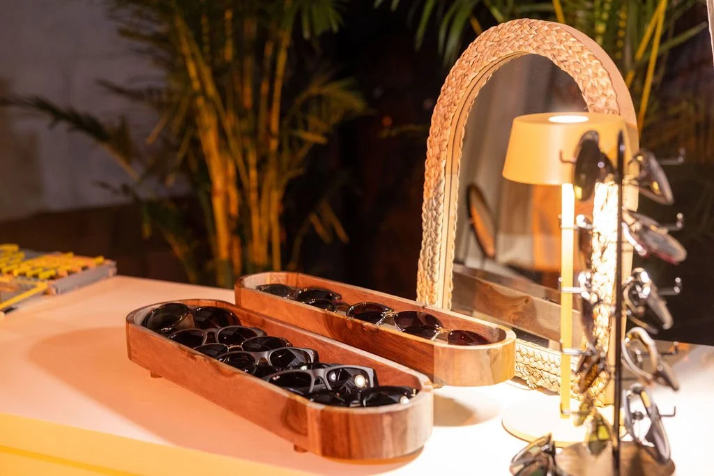 Sunglasses sit in round wooden trays in front of a mirror