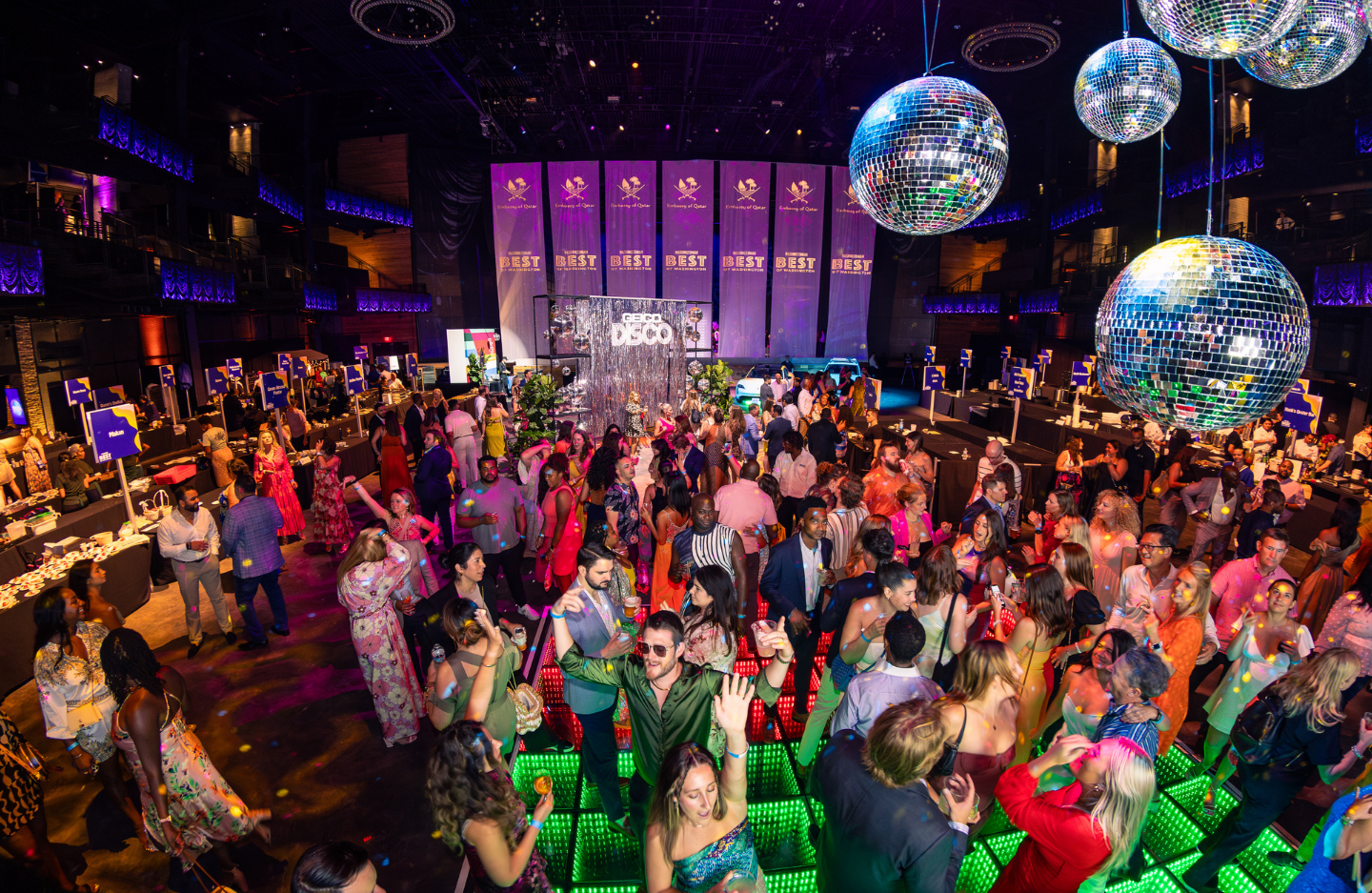 Event attendees dance on the dance floor and mingle around the space under disco balls and colorful lights at the Best of Washington event.