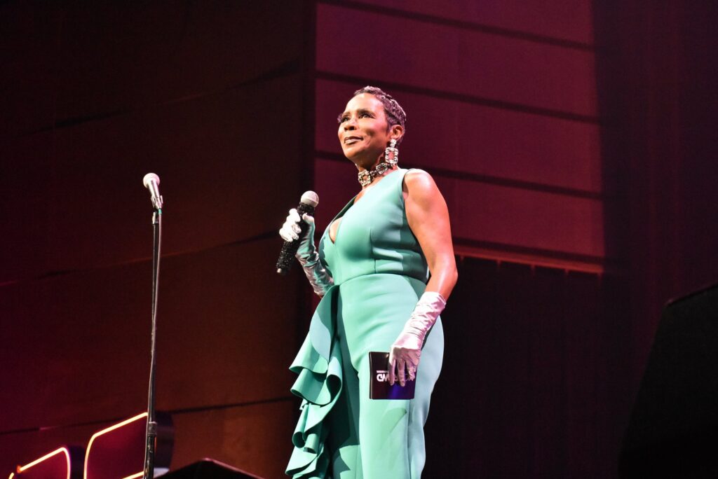 A woman holds a mic onstage at the 2025 "Because They're Funny" Comedy Festival