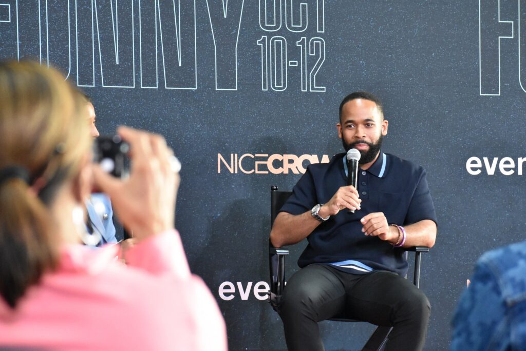 A woman photographs a man holding a mic at the 2025 "Because They're Funny" Comedy Festival