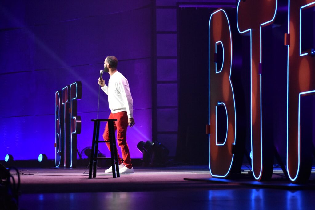 A man holds a mic onstage at the 2025 "Because They're Funny" Comedy Festival