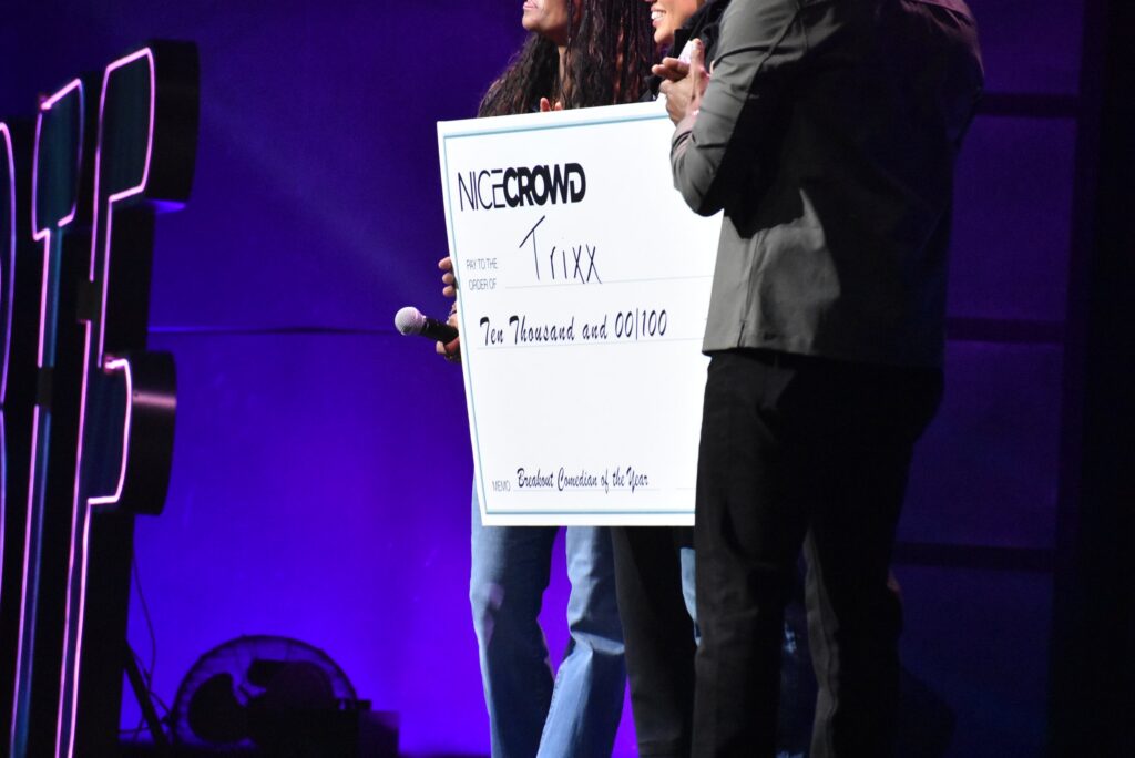 Onstage presenters hold an oversized check from NICE CROWD to "Trixx" for ten thousand dollars, as the award for "Breakout Comedian of the Year", at the 2025 "Because They're Funny" Comedy Festival