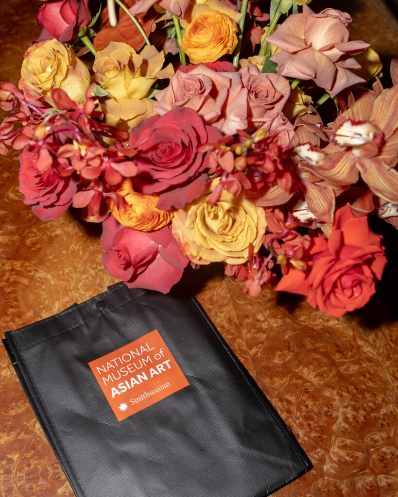 A bouquet of red and yellow flowers and a small black bag with the National Museum of Asian Art logo on it