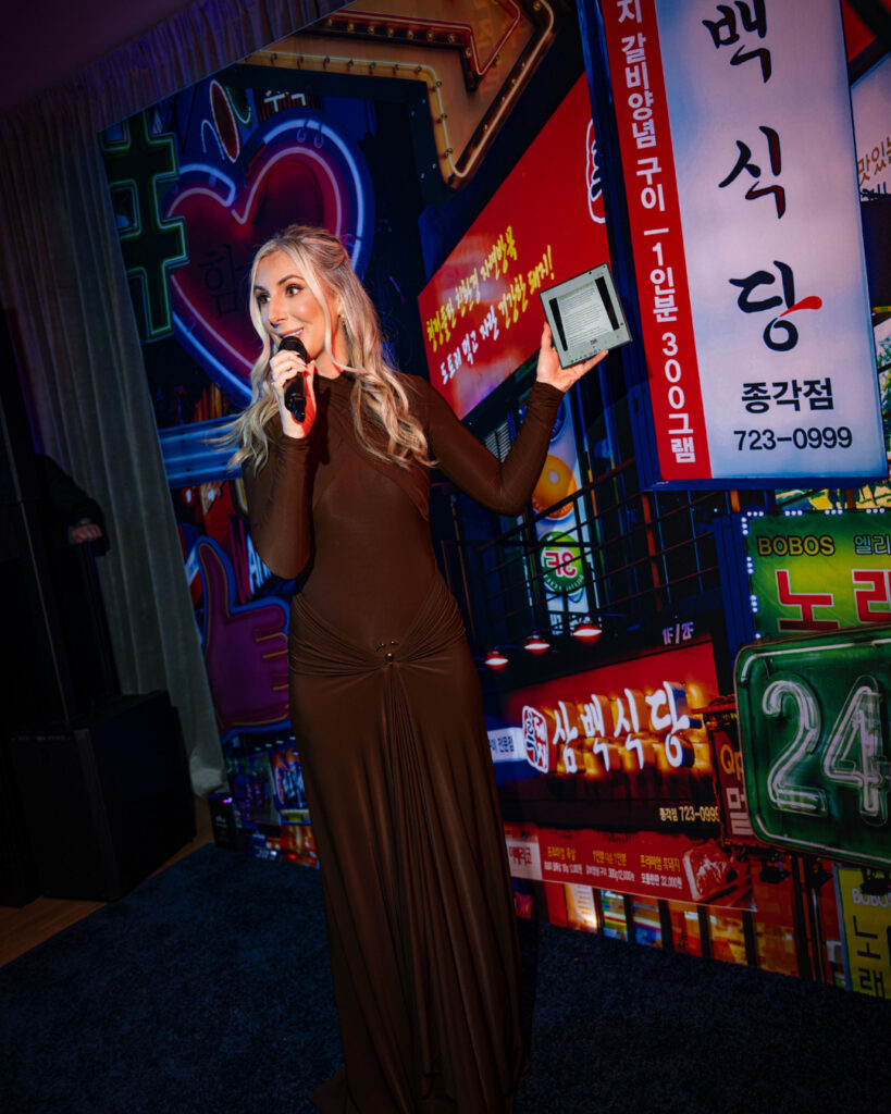 A woman stands onstage speaking into a mic