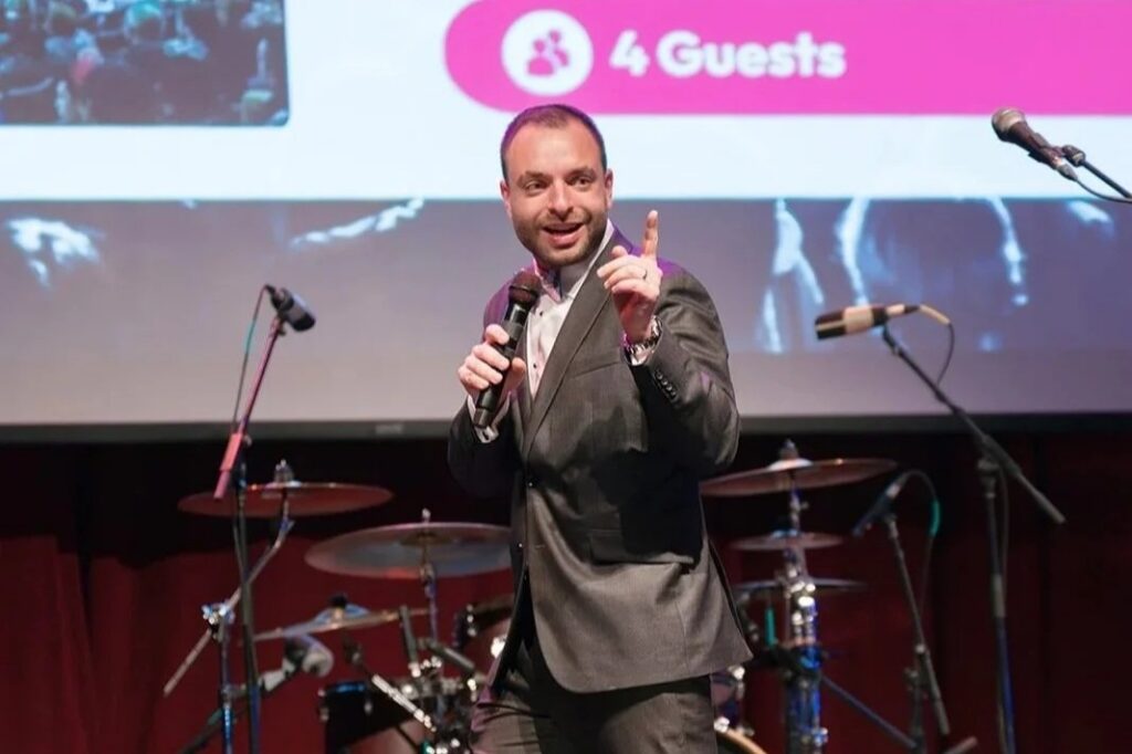 A man holds a mic onstage at the Paths for Families Gala