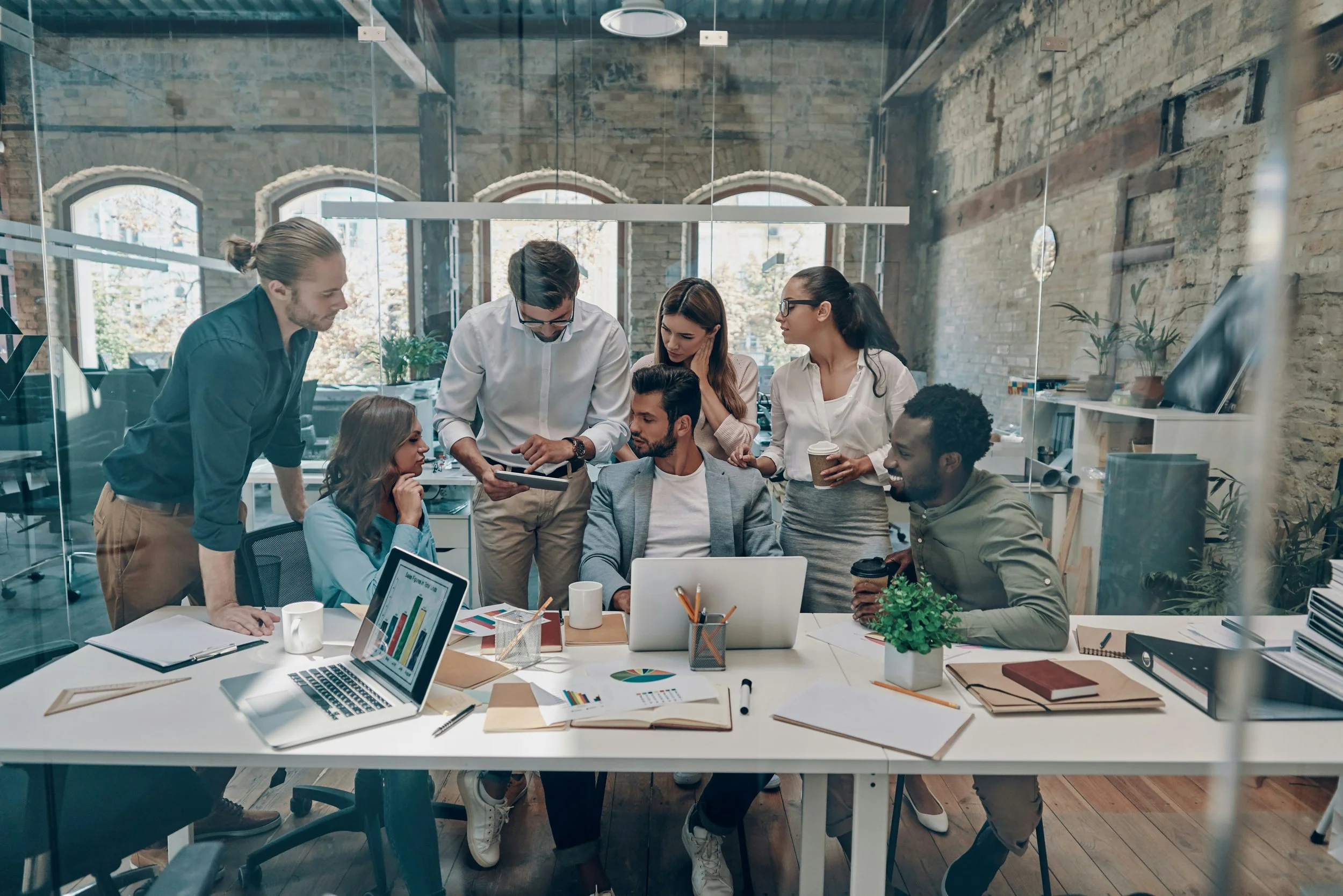 A group of people huddle around a table in an office, brainstorming together.