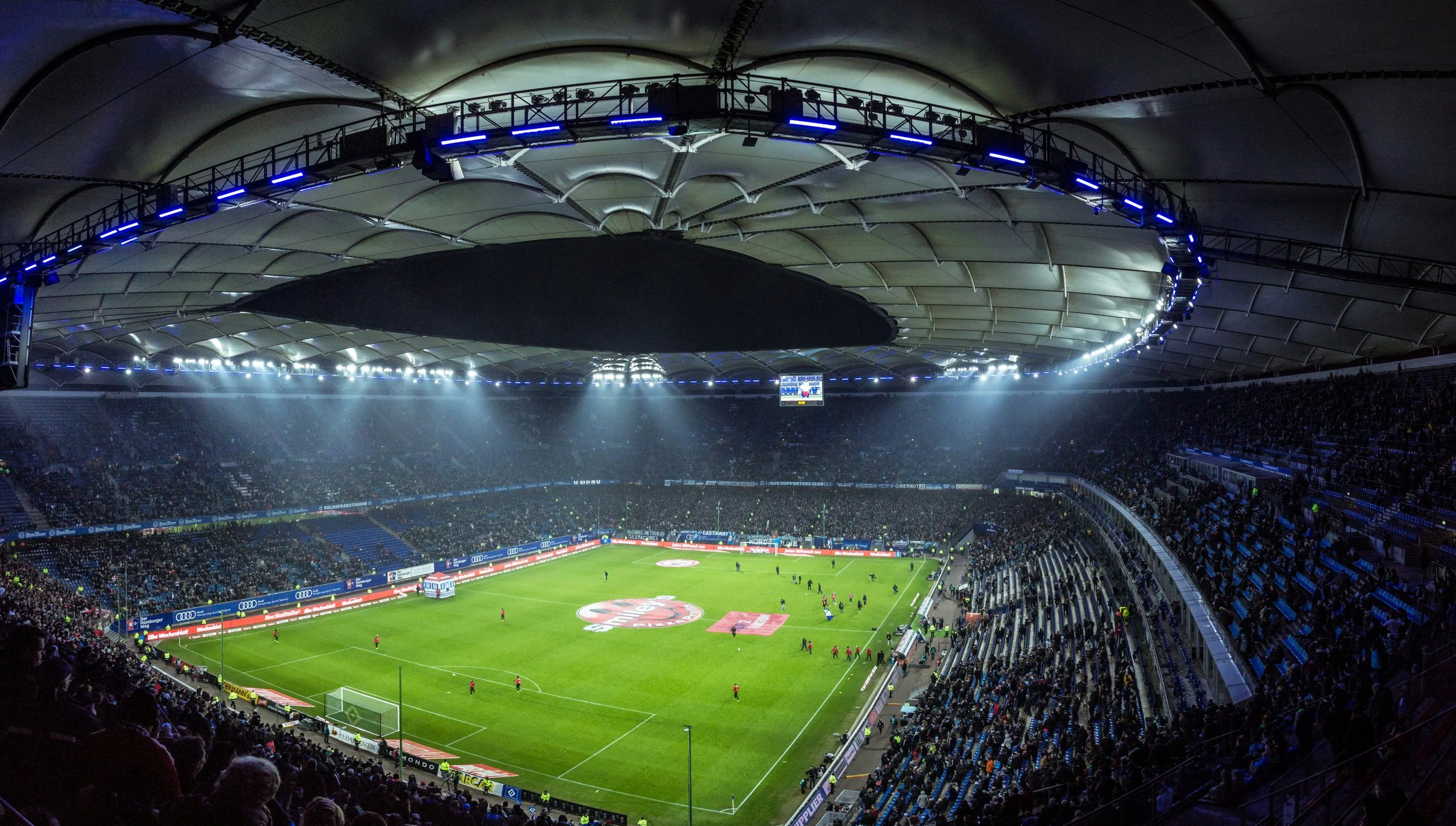 A soccer game in a huge stadium, photographed from high in the back row of seats.