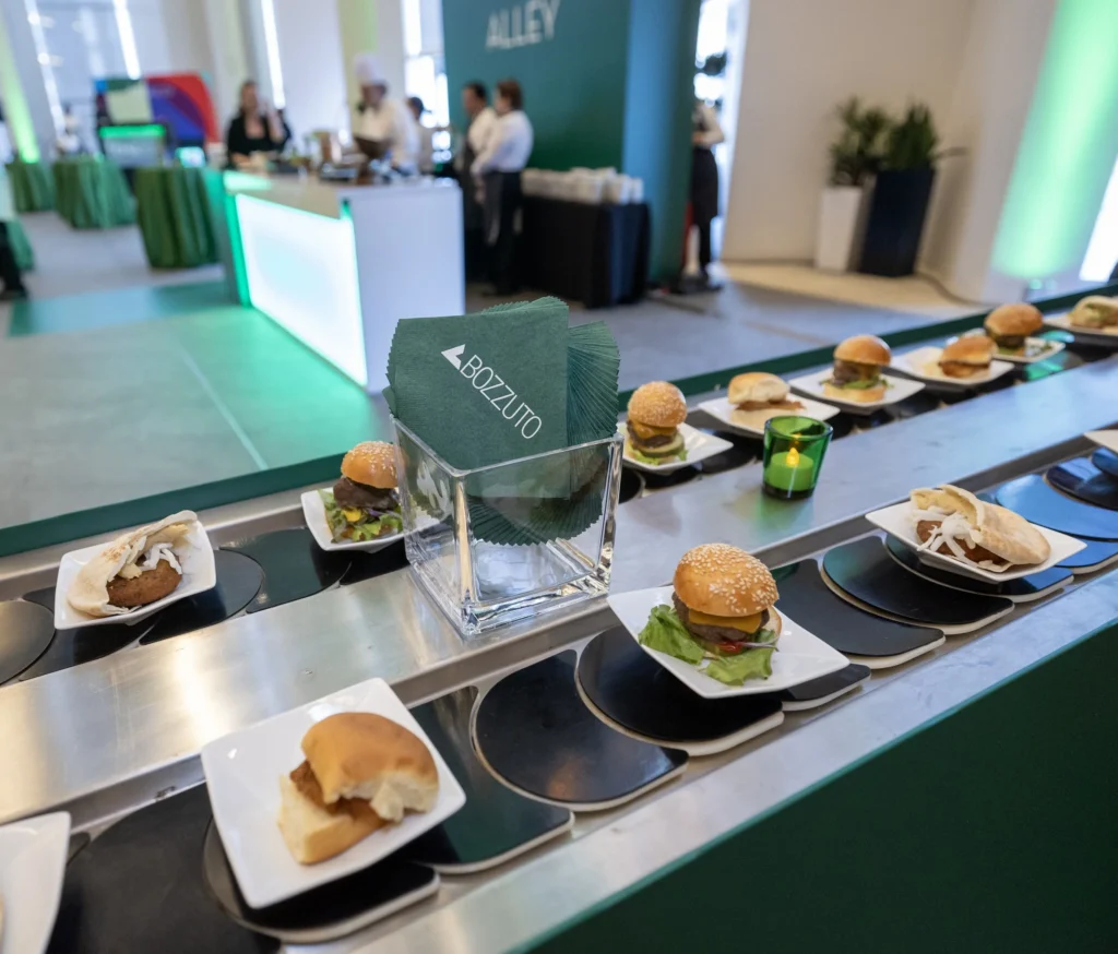 A food conveyor circles around an arrangement of green napkins with the Bozzuto logo on them.