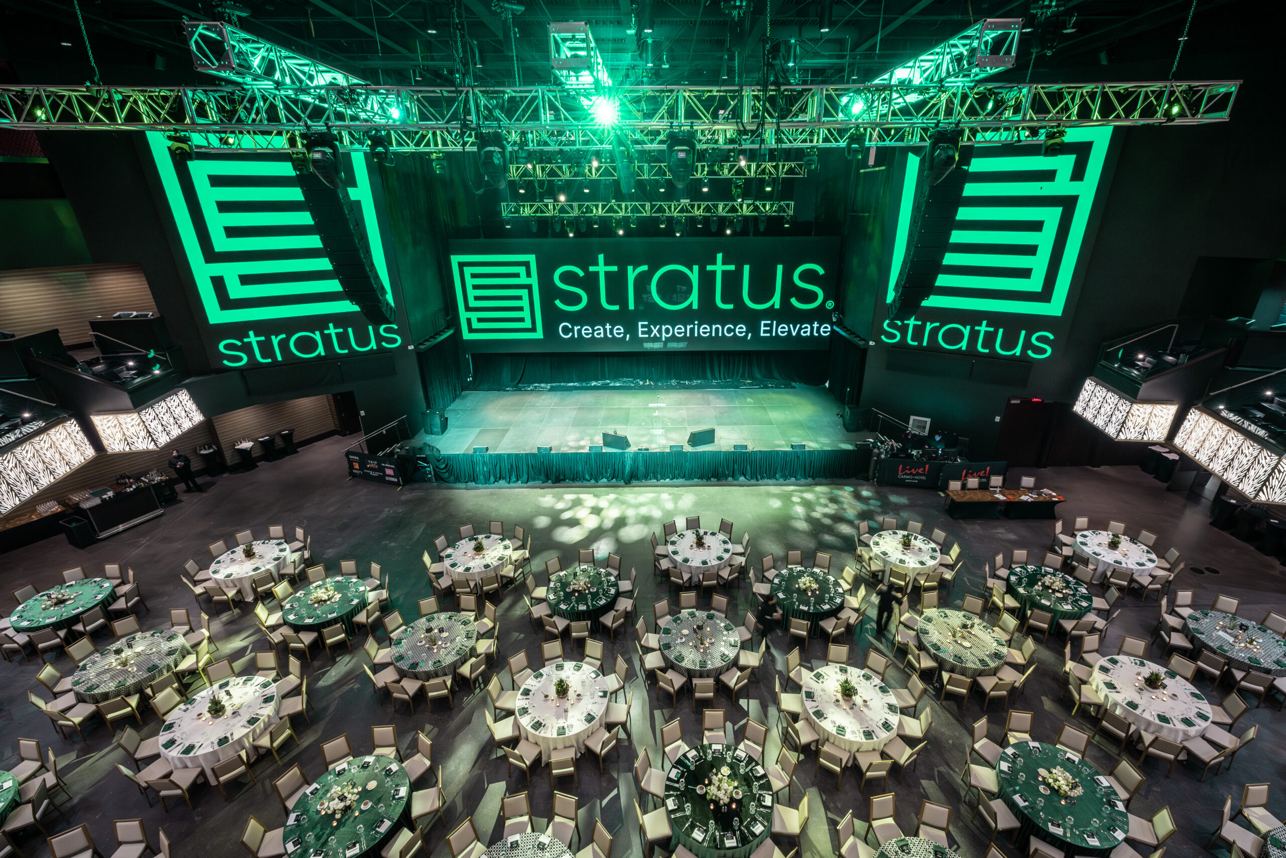 White and green tables and chairs fill a space in front of a large stage with the Stratus logo and tagline displayed prominently in green lights.