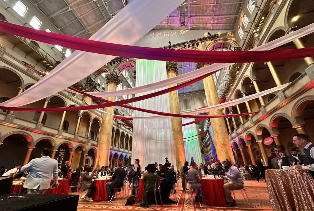 Elegant red and white fabrics drape across the space above guests seated at tables with red and sparking gold tablecloths.