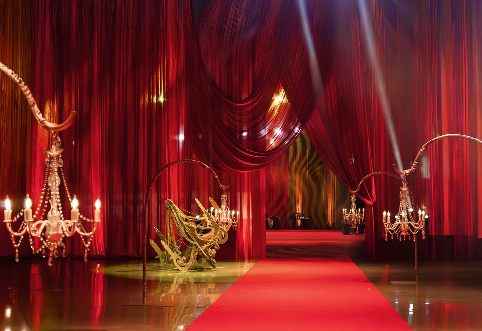 Chandeliers hang low among red carpets and semi-transparent red curtains.