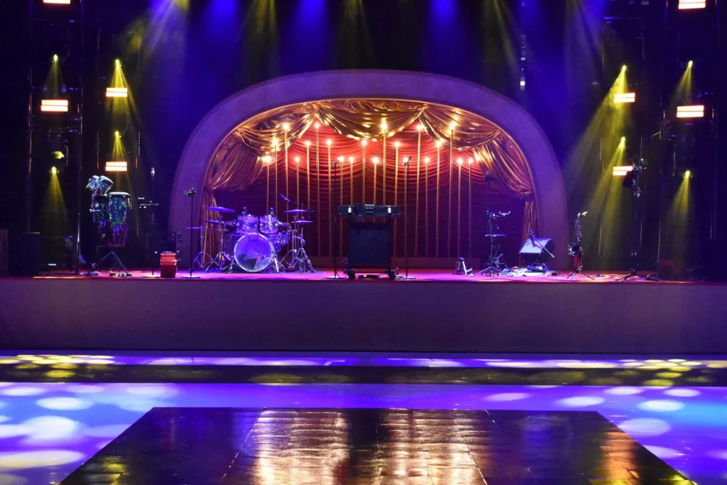 An empty stage with instruments awaiting performers, under purple and yellow lights