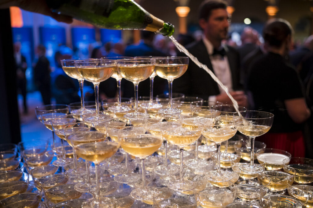 A bottle of champagne is poured into glasses arranged in a tower.