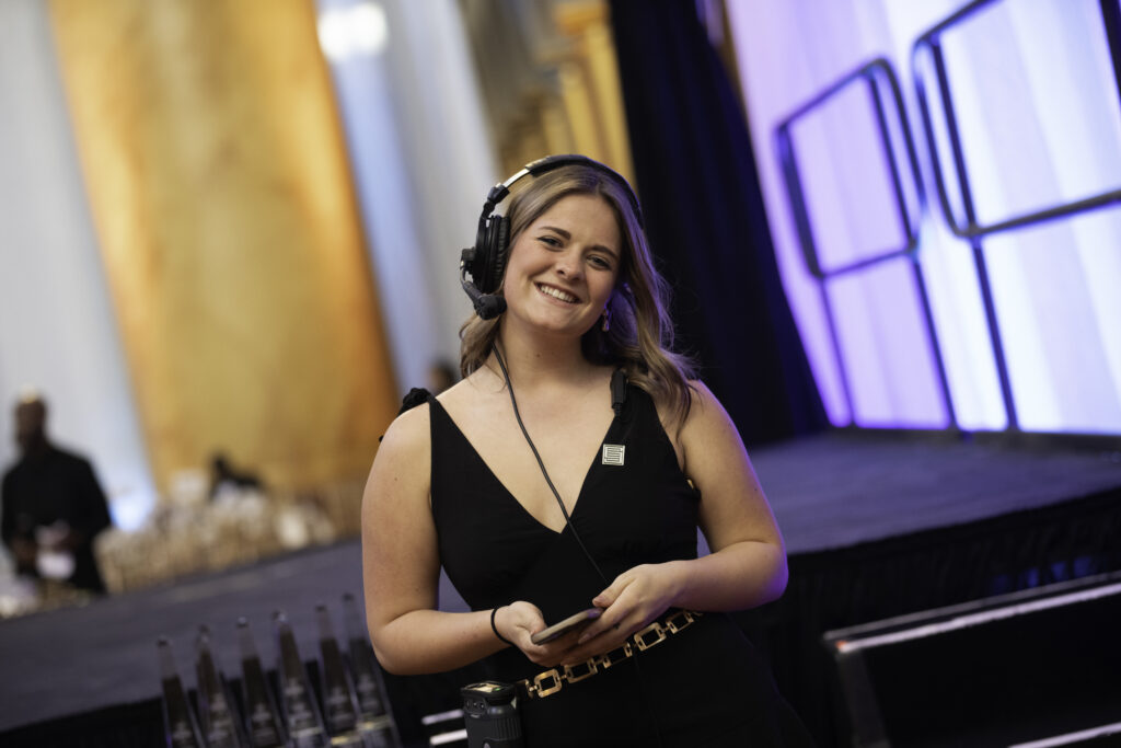 A Stratus intern stands next to a stage wearing a headset and smiling.