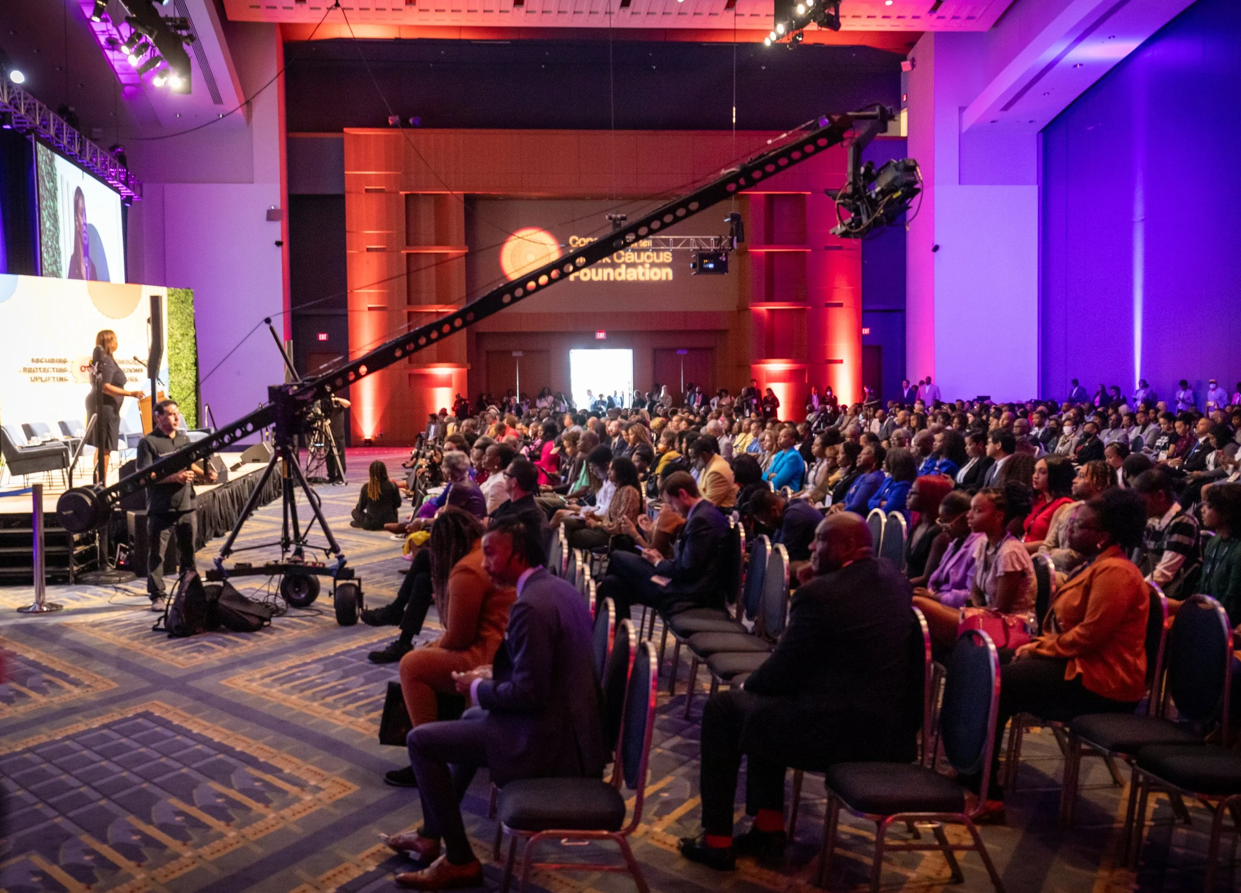 An audience sits in front of a stage as event staff operate a camera on a crane at the Congressional Black Caucus Foundation.