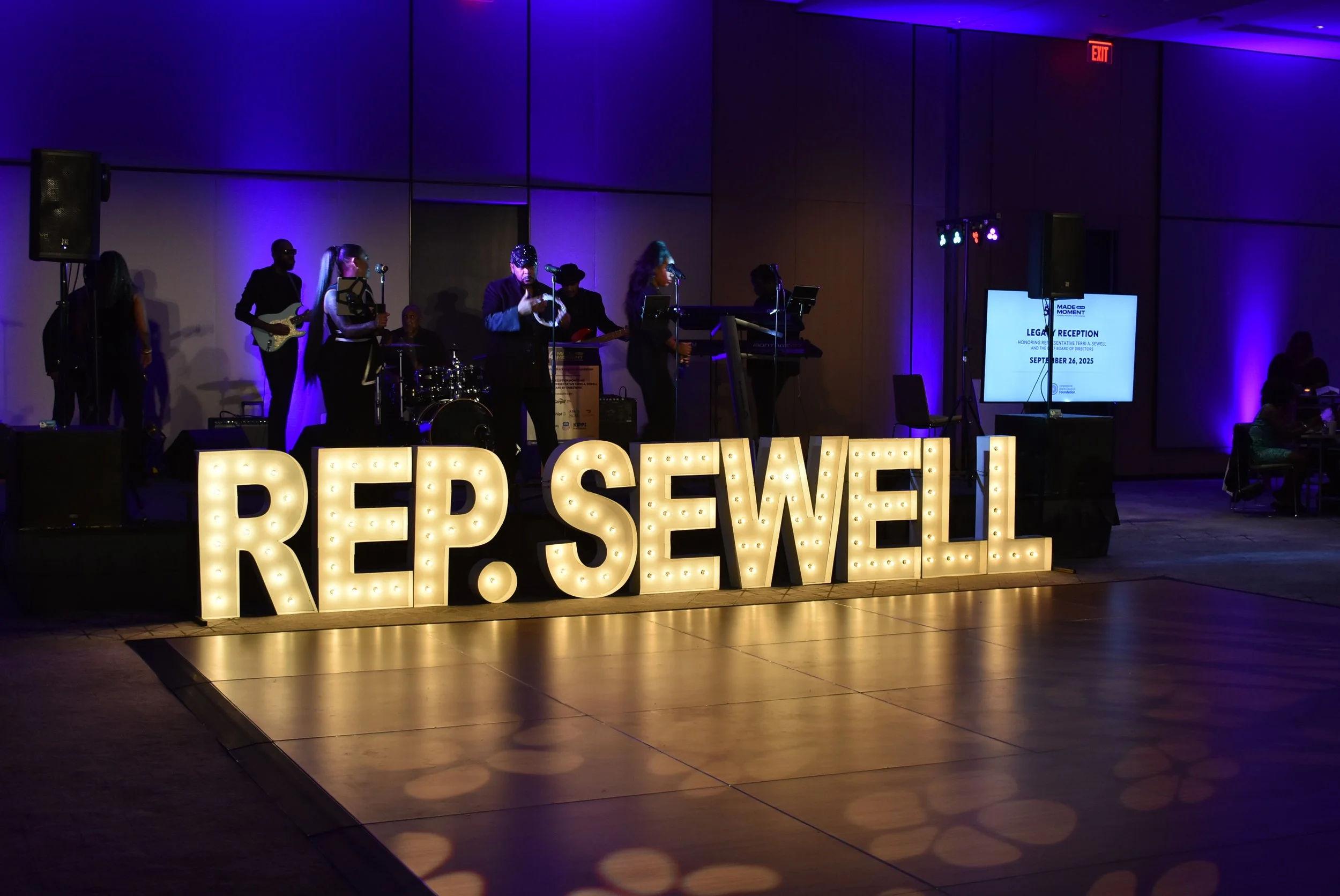 A band plays on a stage behind a lighted sign that reads "Rep. Sewell".