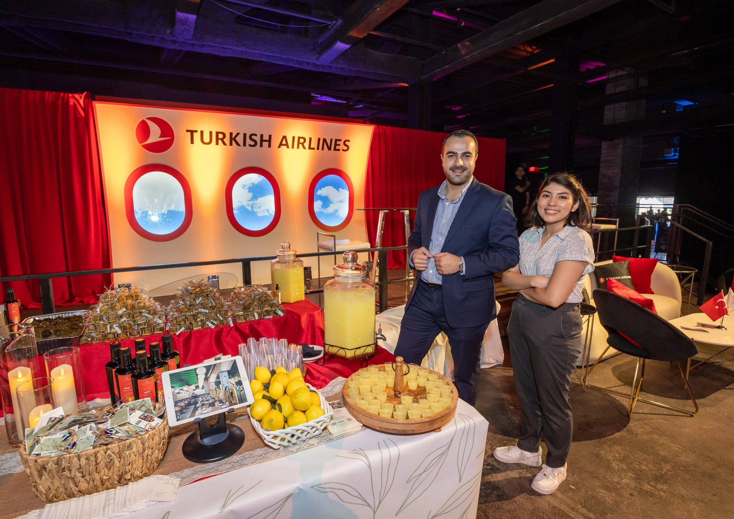 Two people pose next to a table of food and drinks at a Turkish Airlines event.